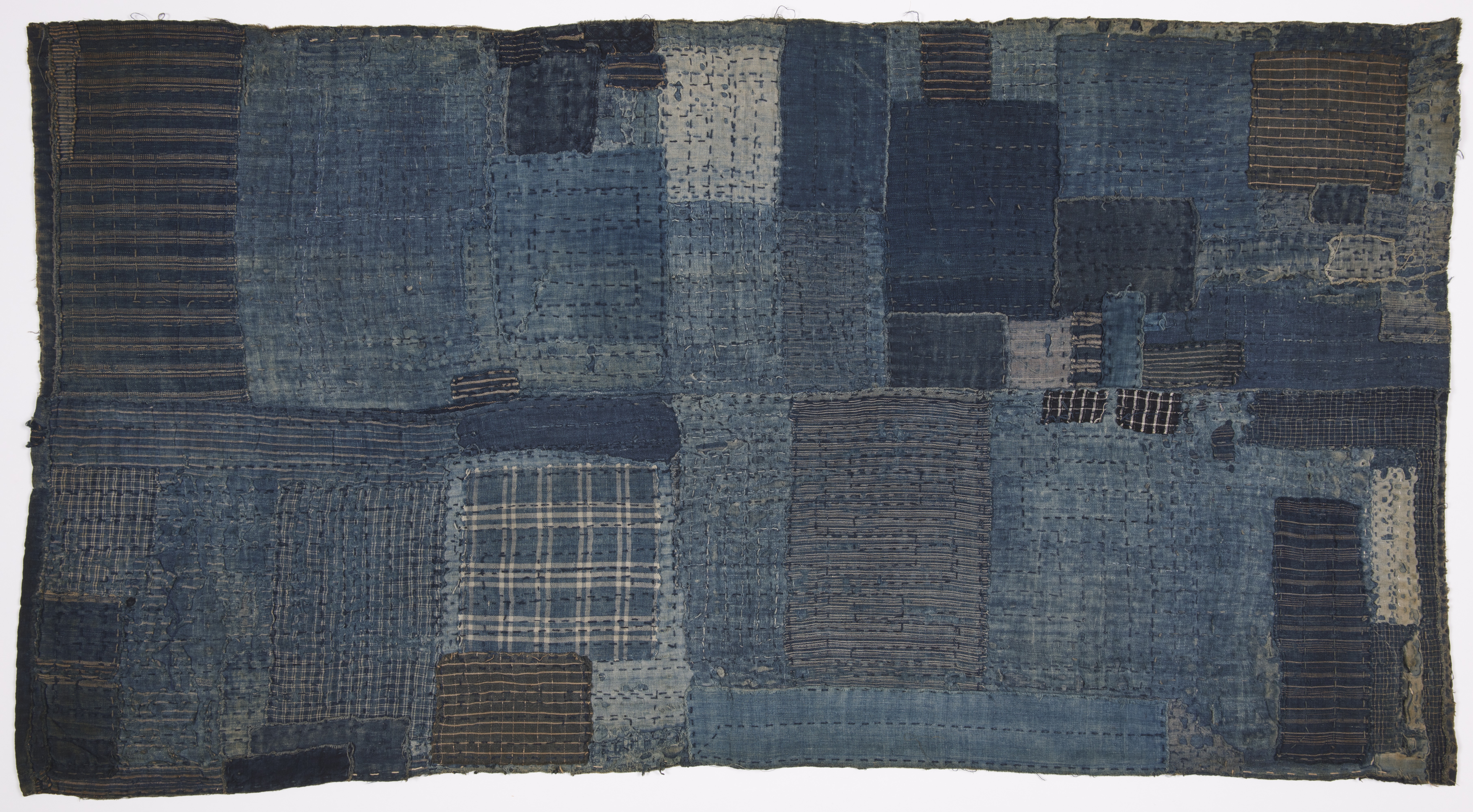 Rectangular sleeping mat pieced from faded blue cotton, with striped and checked patches and dense visible stitching.