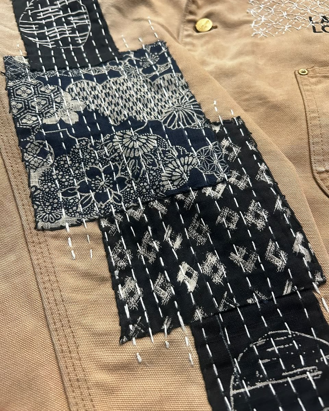 Close detail of black patterned textile patches held with white running stitches.