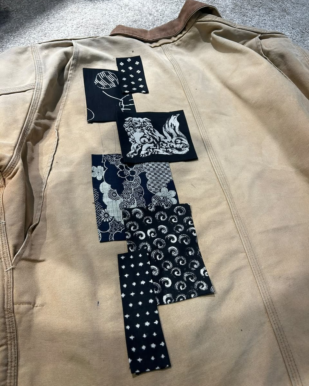 Dark textile patches placed on the tan jacket before the visible stitches are completed.