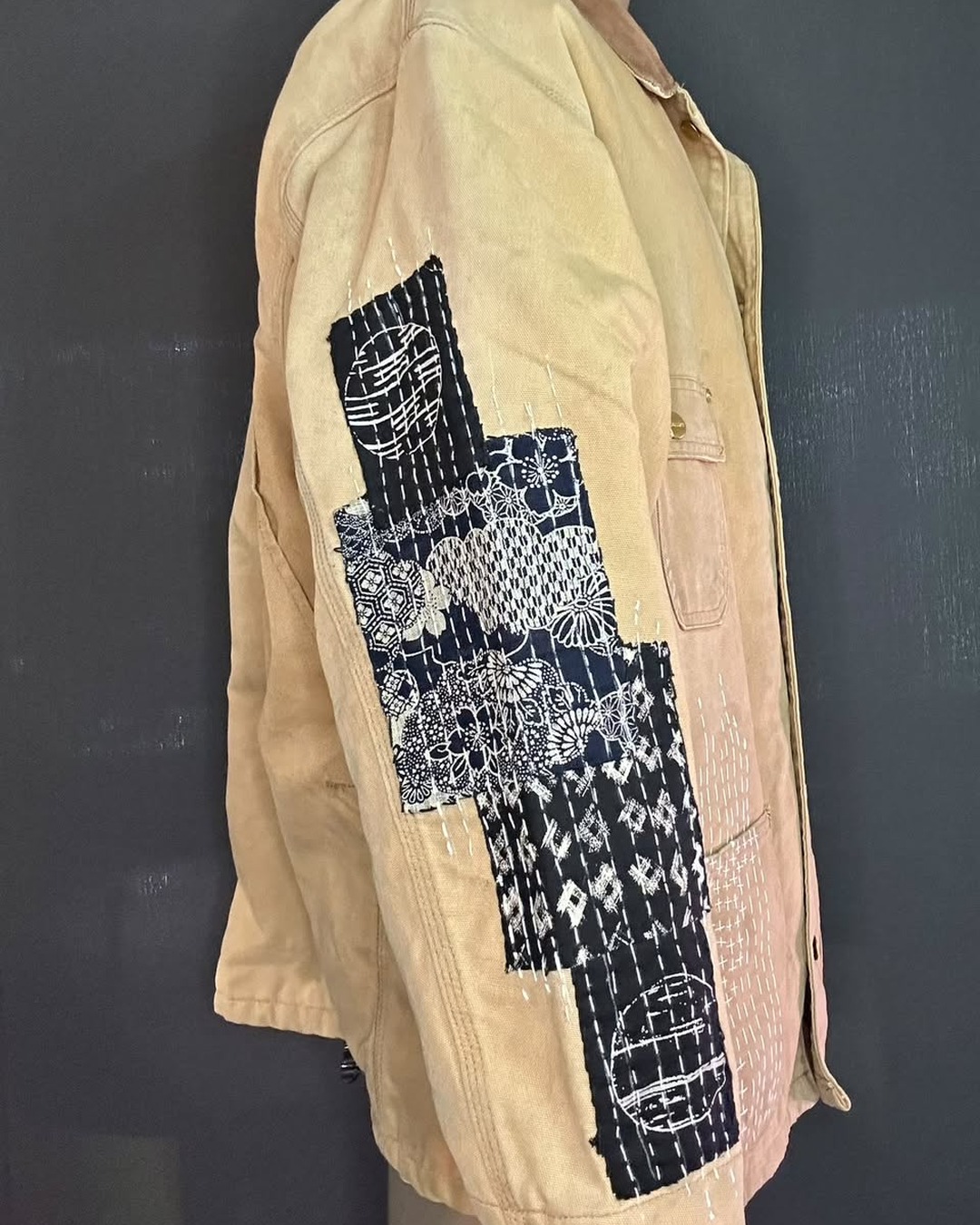 Side view of the tan jacket showing the black patchwork panel running down the sleeve.